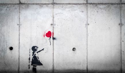 image on concrete wall of small girl with arm outstretched, reaching toward a red heart-shaped ballon that has slipped from her grasp